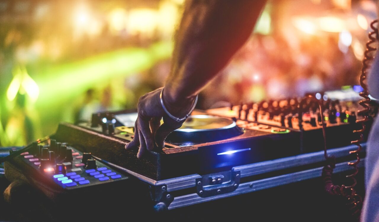 Dj mixing outdoor at beach party festival with crowd of people in background